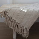 A cream cotton throw/bedspread with tassels.