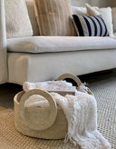 A beige cotton mache round tray with decorative handles.