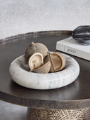 A round white and gray marble bowl filled with dried seed pods, styled on a dark round table next to a book.