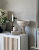 A square-shaped sculpture made of travertine limestone with a fibrous texture, displayed on a white square base.